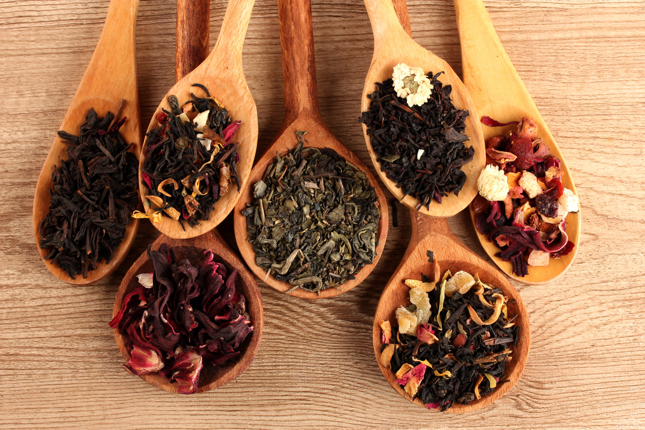 assortment of dry tea in spoons, on wooden background